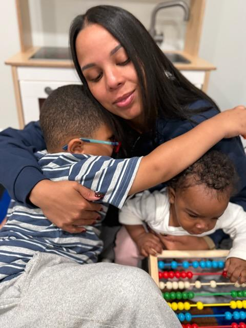 An adult hugging two children while one child plays with a colorful abacus