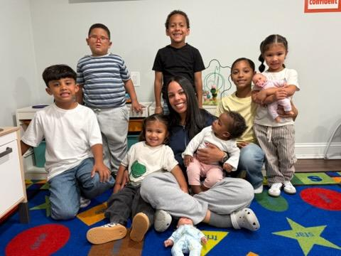 Children and two adults posing together on a colorful classroom rug